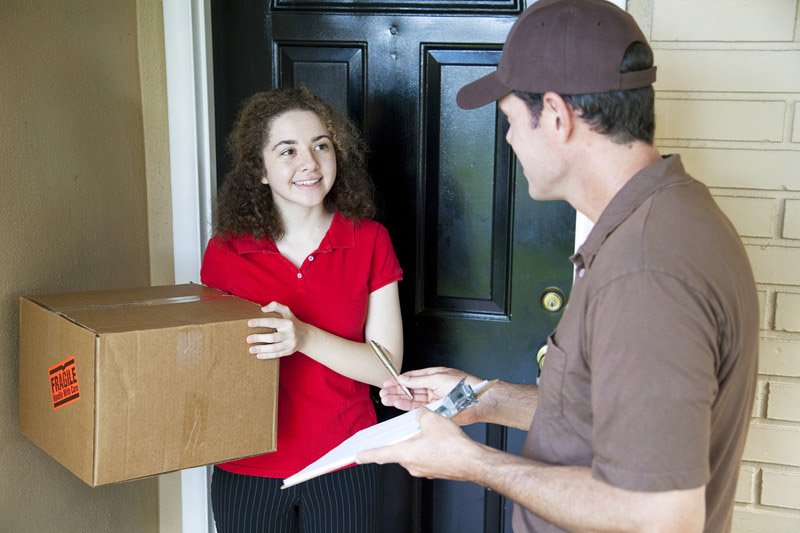 Shows a male courier giving a package to a female British customer